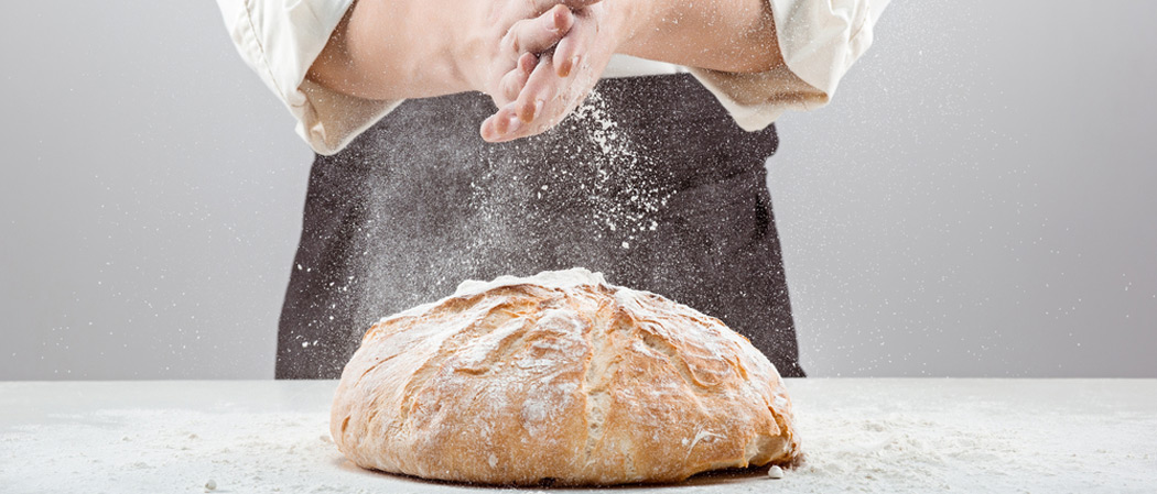 Baker menaburkan tepung di atas roti sourdough