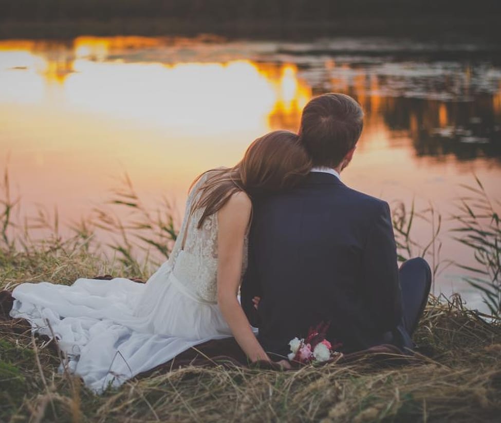 Pengantin duduk di tepi danau saat senja